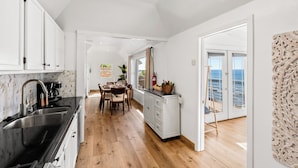 A modern kitchen with a black countertop, white cabinets, and a wooden dining table with chairs. There is a view of the sea through a glass door. - Single Family Beachfront Home with a Spa P2031-0 (Oceanside)