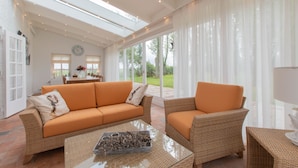 A spacious living room with a large sofa, a smaller armchair, and a coffee table. There is a dining area in the background with a table and chairs. - ‘Prachtig gelegen vrijstaand landhuis met grote zonnige tuin’ (Hansweert)