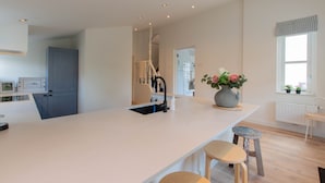 A modern kitchen with a large island, a built-in sink, and a window with a view. - ‘Prachtig gelegen vrijstaand landhuis met grote zonnige tuin’ (Hansweert)