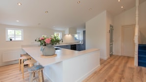 A modern kitchen with a central island, wooden stools, and a vase of flowers. - ‘Prachtig gelegen vrijstaand landhuis met grote zonnige tuin’ (Hansweert)