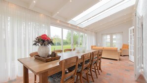 A spacious dining area with a long wooden table, cushioned chairs, and a vase of flowers. - ‘Prachtig gelegen vrijstaand landhuis met grote zonnige tuin’ (Hansweert)