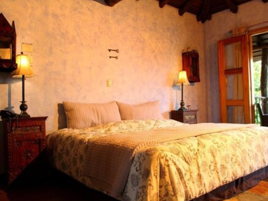 A bedroom with a bed, two bedside lamps, a wooden cabinet, and a window with curtains.