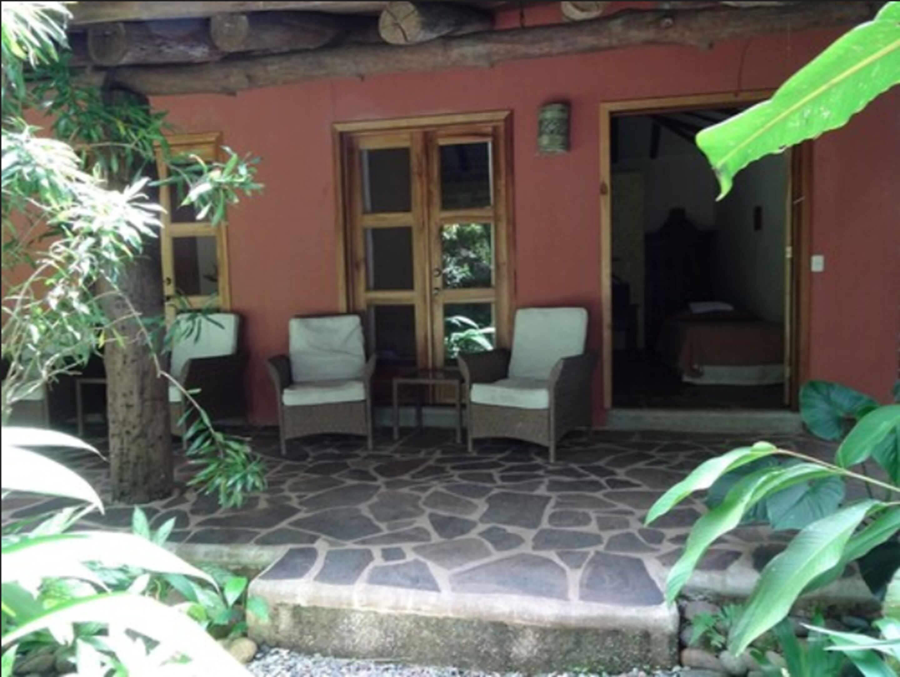Un patio cubierto con suelo de piedra, dos sillas de mimbre y una puerta que da a una habitación interior.