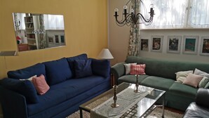 A living room with a blue sofa, a green sofa, a glass coffee table, and a chandelier. - Large three-room apartment with 2 bathrooms for a maximum of 8 people (Kellenhusen)