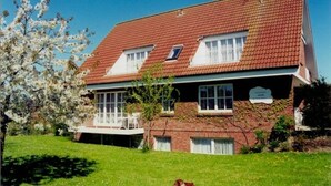 A two-story house with a red-tiled roof, a covered porch, and a brick exterior. - Large three-room apartment with 2 bathrooms for a maximum of 8 people (Kellenhusen)
