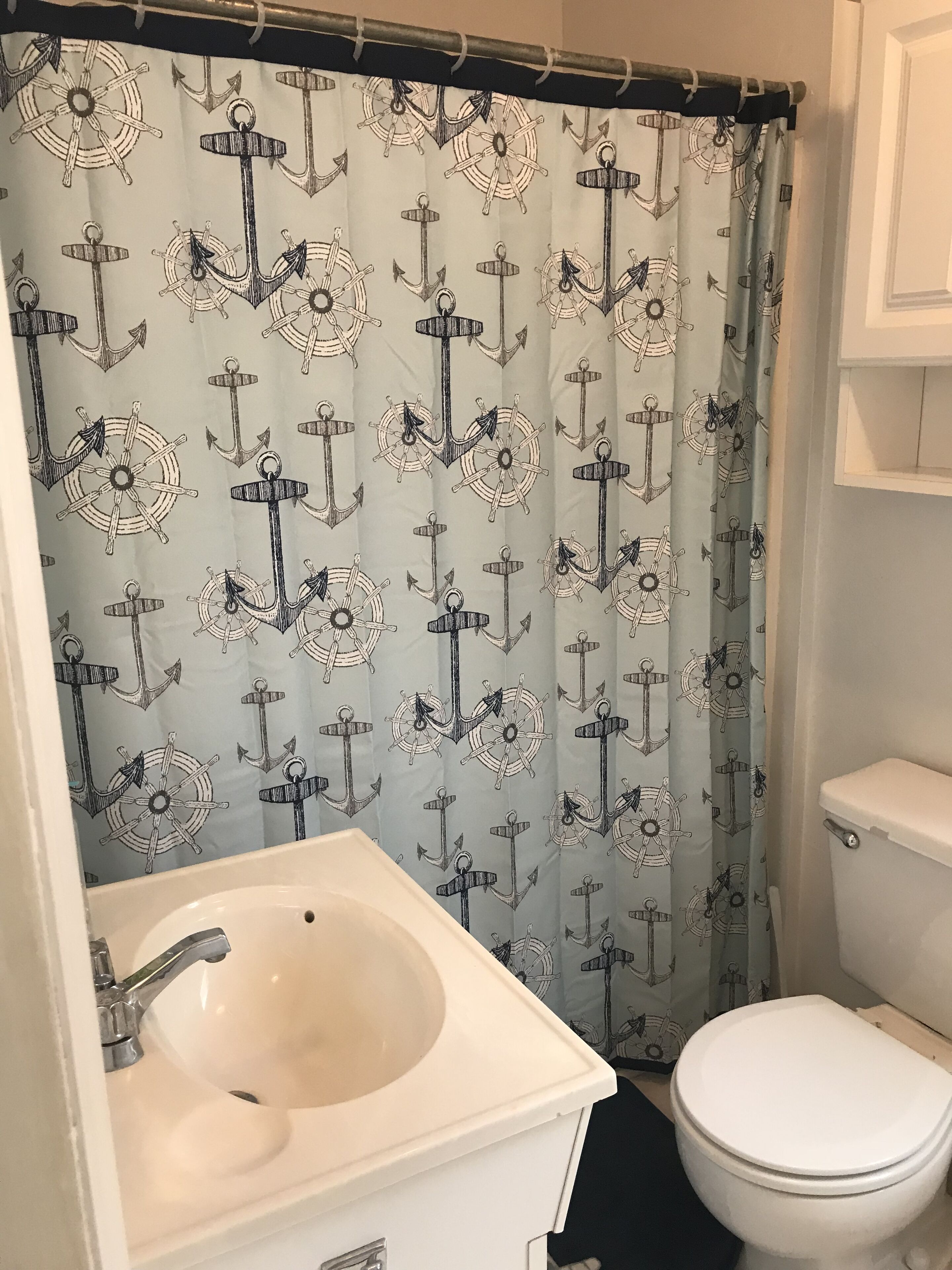 A bathroom with a nautical-themed shower curtain, a white sink, and a toilet.