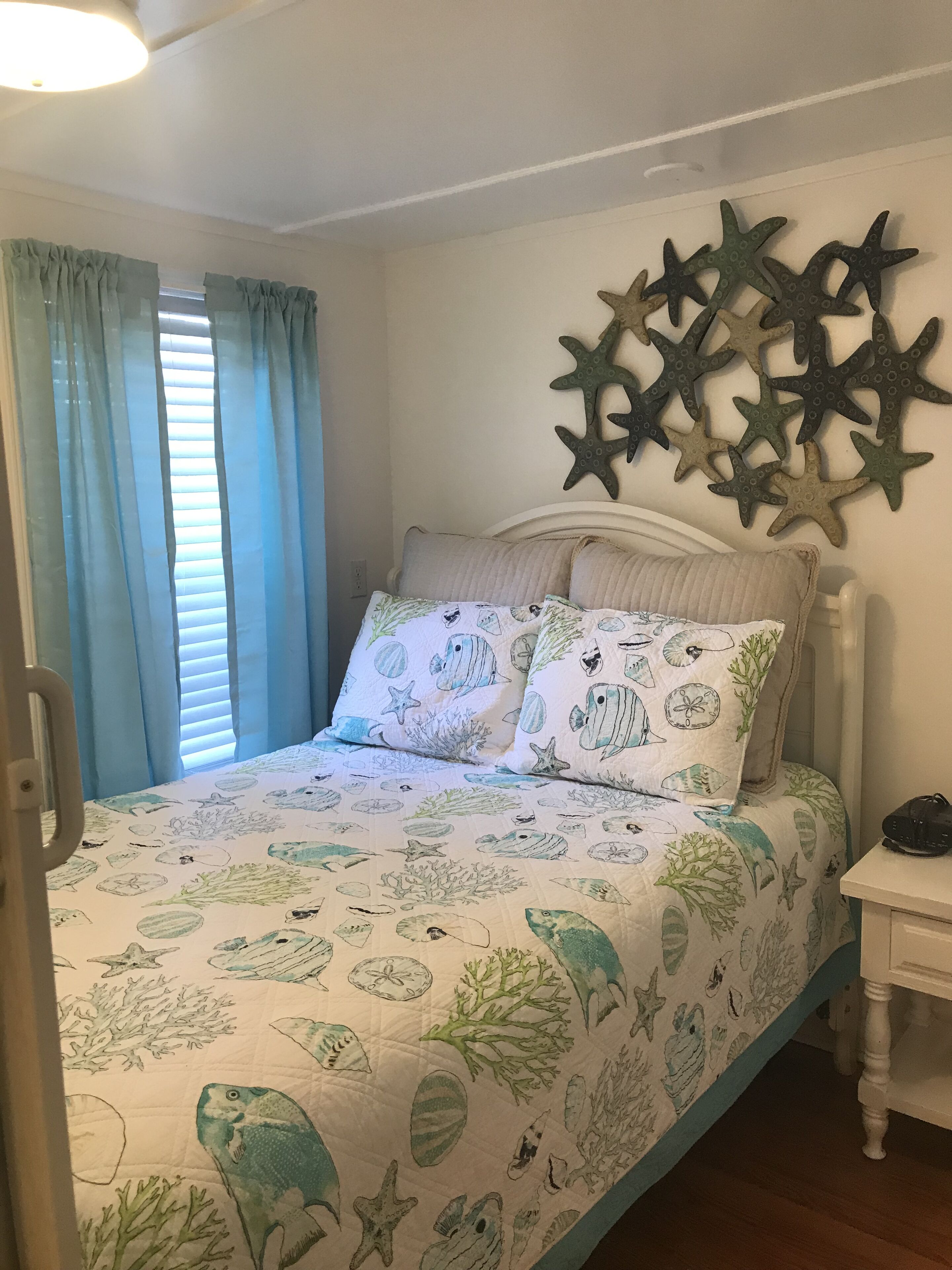 A bedroom with a bed featuring a marine-themed bedspread, a white headboard, and a wall decorated with starfish.