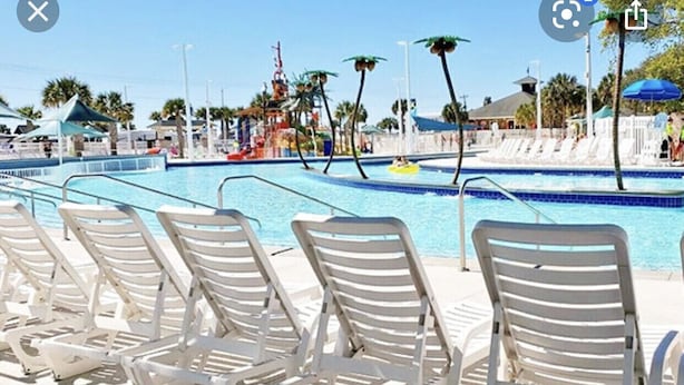 Uma área de piscina com espreguiçadeiras, um toboágua e palmeiras.
