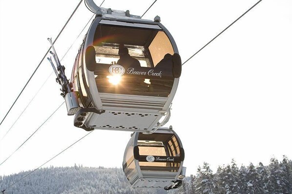 A cable car with "Beaver Creek" branding, suspended by cables, and a snowy landscape below.