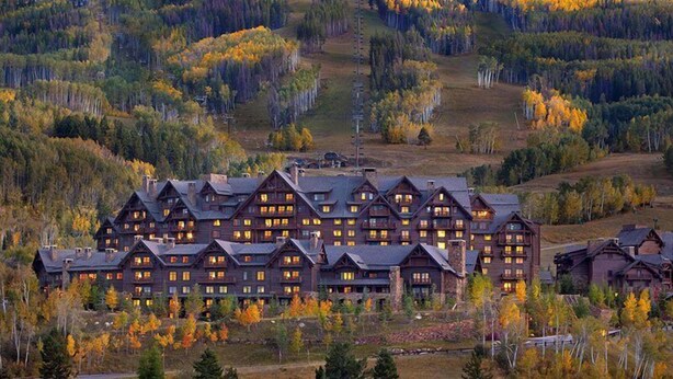 A lodge with multiple floors and a central tower, surrounded by autumn-colored trees. - Bachelor Gulch Ritz-carlton Hotel Room With Ski in, Ski out Access, Hot Tub, and Full Service Spa (Avon)