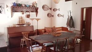 Un comedor con una mesa y sillas de madera, un banco de madera, y un estante fijado a la pared con objetos decorativos.