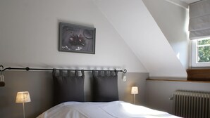 Une chambre avec un plafond en pente, un lit recouvert d’une courtepointe à motifs floraux, deux lampes de chevet et une œuvre d’art encadrée au-dessus du lit.