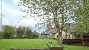 A wooden bench in a grassy yard with a tree and a house in the background. - Luxury Home in Gouvy With Pool & Sauna (Gouvy)