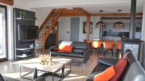 En moderne stue med pejs, fjernsyn og spiseplads med orange stole.