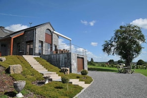 A modern house with a stone facade, a wooden staircase, and a gravel driveway.