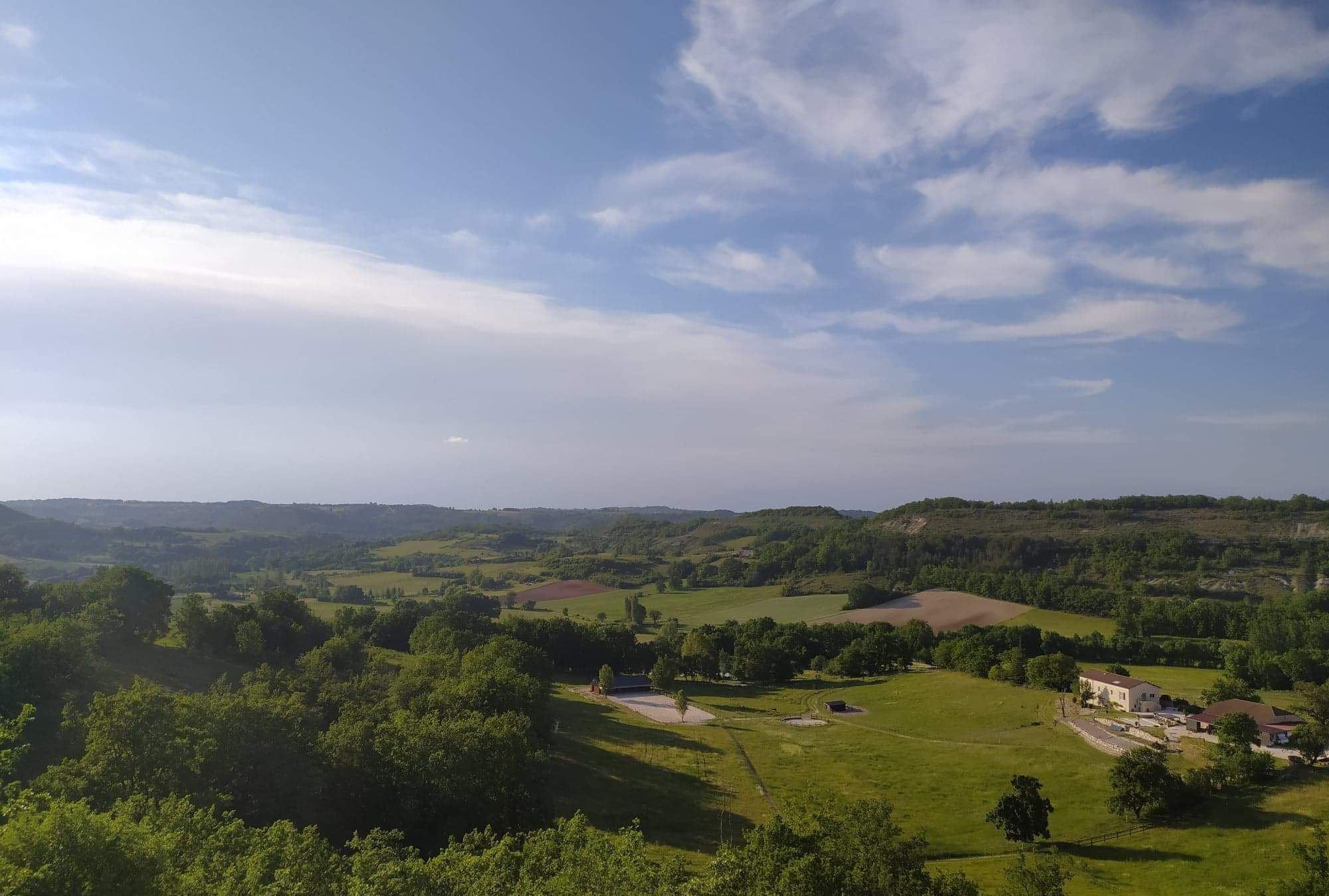 Un paysage rural caractérisé par des collines douces, quelques bâtiments dispersés et un ciel dégagé.