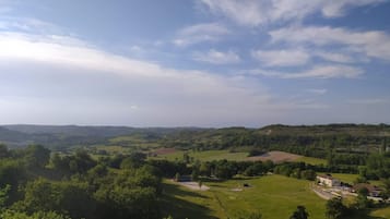Un paysage rural caractérisé par des collines douces, quelques bâtiments dispersés et un ciel dégagé.