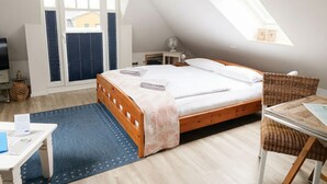 A bedroom with a sloped ceiling, a bed with a wooden frame, a small bedside table, a chair, and a desk with a chair. - Apartment at the Rosenhof T301 - T301 (Kühlungsborn)