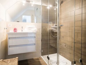 Un baño moderno con cabina de ducha de vidrio, un tocador blanco con espejo y piso de madera.