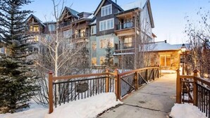 A multi-story lodge with a wooden deck leading to the entrance, surrounded by snow-covered ground and trees. - Spacious 4 Bedroom Vacation Rental in Convenient Location with Scenic Views, Pool, Hot Tub (Breckenridge)