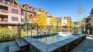A swimming pool with a stone border, surrounded by a metal fence, and adjacent to multi-story buildings with balconies. - Spacious 4 Bedroom Vacation Rental in Convenient Location with Scenic Views, Pool, Hot Tub (Breckenridge)