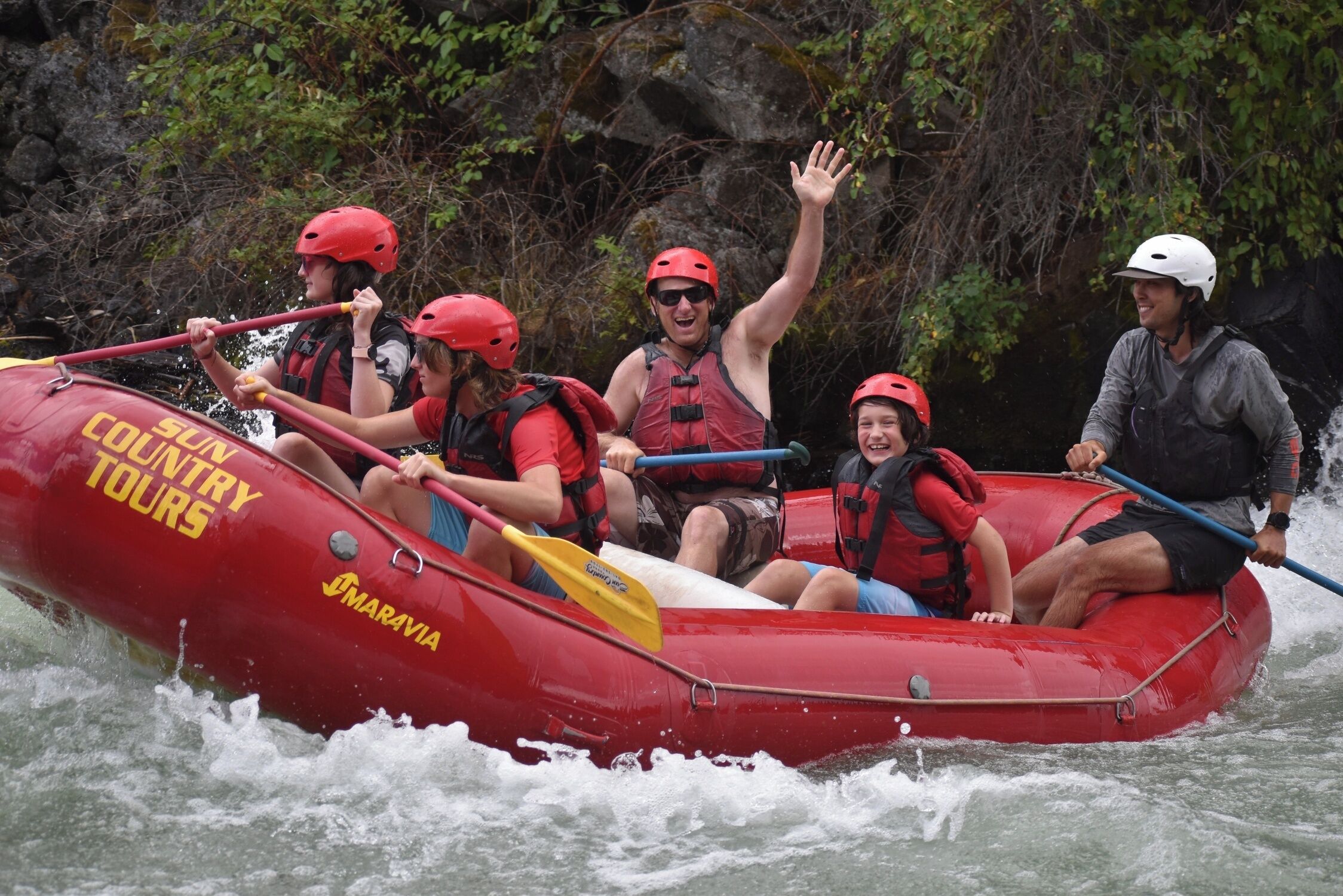 A group of people in a red inflatable raft with 'Columbia Country Tours' written on it, navigating through water.