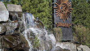 A waterfall and a sign with the word "SUNRIVER" and a sun symbol. - LIVE LODGE LIFE- Upscale decor, sleeps 15, hot tub, bikes, 10x SHARC, amazing!! (Sunriver)
