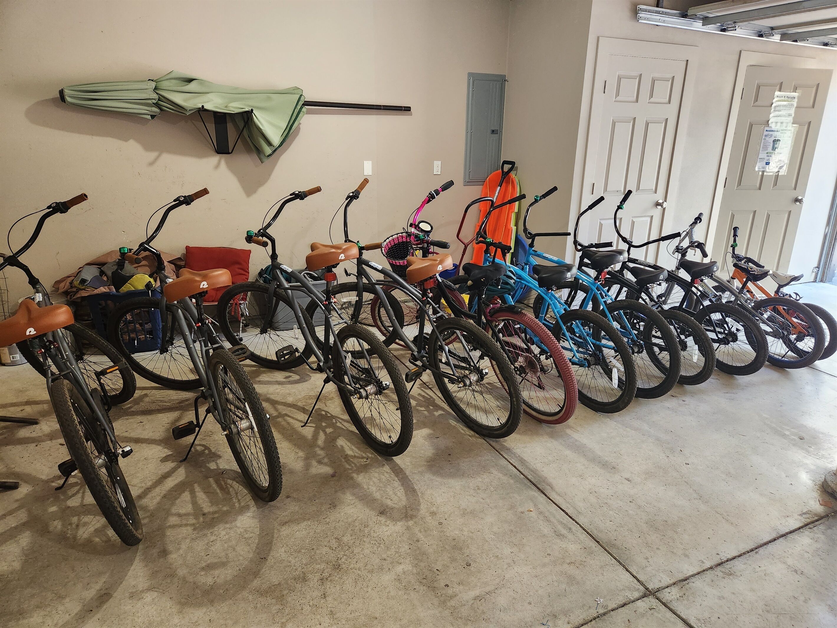 A row of bicycles parked indoors, with a green umbrella and a blue bicycle leaning against the wall.
