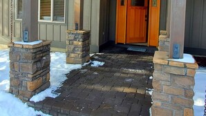 A building with a covered entrance, stone pillars, and a wooden door. - LIVE LODGE LIFE- Upscale decor, sleeps 15, hot tub, bikes, 10x SHARC, amazing!! (Sunriver)