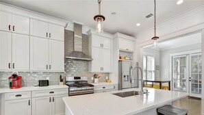 A modern kitchen with white cabinetry, a central island, stainless steel appliances, and pendant lighting. - Ocean Oaks 19 - gorgeous home only a short walk to pool and beach (Jekyll Island)