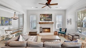 A spacious living room with a fireplace, a ceiling fan, and a dining area with a table and chairs. - Ocean Oaks 19 - gorgeous home only a short walk to pool and beach (Jekyll Island)