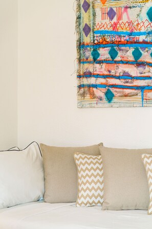 Une pièce avec un canapé blanc, deux coussins à motifs et un tableau abstrait aux couleurs vives accroché au mur.