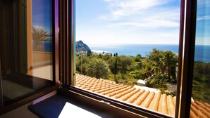A room with a large window overlooking a coastal landscape, including a mountain and the sea. - TRAMONTO: exclusive and panoramic apartment with sea-sunset view in Ischia (Forio)