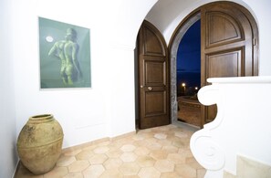 Un couloir orné d’un grand vase, d’une œuvre d’art encadrée et d’une porte en bois donnant sur un balcon.