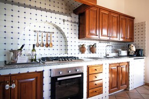 A kitchen with wooden cabinets, a stove, and a tiled backsplash. - TRAMONTO: exclusive and panoramic apartment with sea-sunset view in Ischia (Forio)