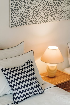 A bed with two pillows, one plain and one with a zigzag pattern, a bedside lamp, and a wall with a polka dot design.