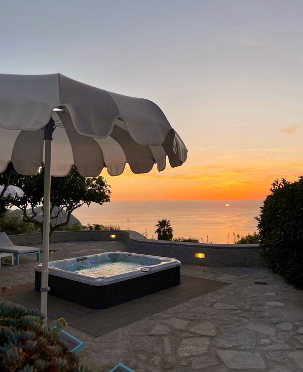 A hot tub with a sunset view, stone patio, and outdoor seating. - TRAMONTO: exclusive and panoramic apartment with sea-sunset view in Ischia (Forio)