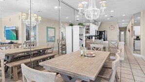 Un comedor con mesas y bancos de madera, una araña y una cocina al fondo.