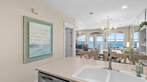 Una cocina con una isla grande, un comedor con muebles de madera, una araña y un cuadro en la pared.