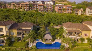 Un resort con varias edificaciones de dos pisos, una piscina central y abundante vegetación.