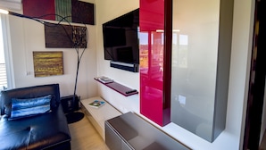A modern living room with a black leather sofa, a flat-screen TV mounted on the wall, and a red cabinet. - Los Suenos Resort Miramar 5B (Jacó)