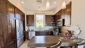 A modern kitchen with dark wood cabinets, stainless steel appliances, and a central island with chairs. - Los Suenos Resort Miramar 5B (Jacó)