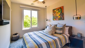 A bedroom with a bed, a ceiling fan, a window, a painting, and a bedside table. - Los Suenos Resort Miramar 5B (Jacó)