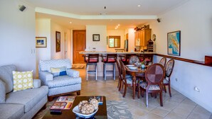 A living room with a sofa, coffee table, and a dining area with chairs and a table. - Los Suenos Resort Del Mar 3C (Jacó)