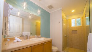 A bathroom with a beige vanity, a white sink, a mirror, and a glass-enclosed shower. - Los Suenos Resort Del Mar 4N (Jacó)