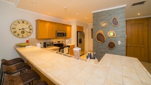 A modern kitchen with a large island, wooden cabinets, stainless steel appliances, and a unique wall decor. - Los Suenos Resort Del Mar 4N (Jacó)
