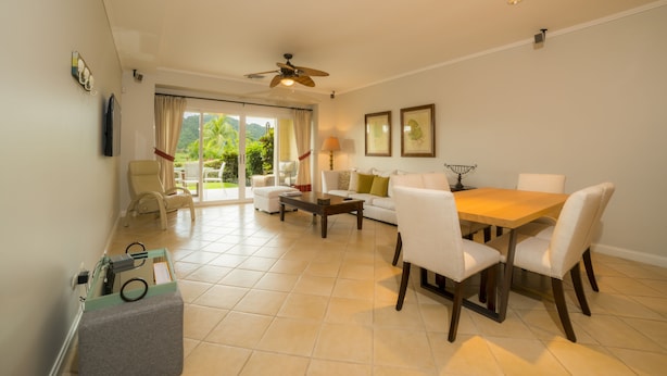 A spacious living area with a dining table, chairs, and a ceiling fan. There is a television mounted on the wall and a window with curtains. - Los Suenos Resort Del Mar 4N (Jacó)