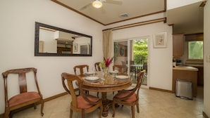 A dining area with a round wooden table, six chairs, a ceiling fan, a large mirror, and a view of the kitchen and outdoor patio. - Los Suenos Resort Veranda 1C (Jacó)
