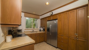 A kitchen with wooden cabinets, a stainless steel refrigerator, a built-in oven, and a window with a view of greenery. - Los Suenos Resort Veranda 1C (Jacó)