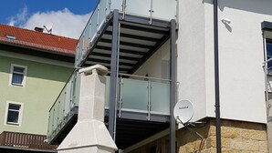 Une maison moderne dotée d’un balcon, de murs en pierre et surplombant un ciel d’un bleu éclatant.